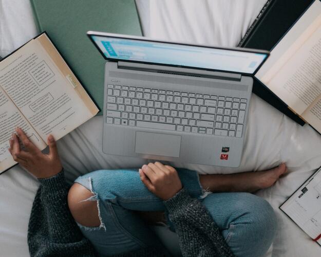 Person sat in bed reading and using laptop