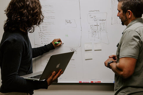 Two people working at a whiteboard, discussing an idea