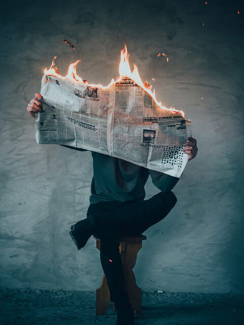 Person, sitting on stool, reading burning newspaper