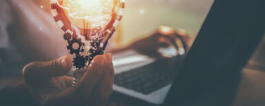 Person working at laptop while holding a lightbulb